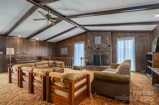 carpeted living room with ceiling fan, vaulted ceiling with beams, a textured ceiling, a brick fireplace, and wood walls