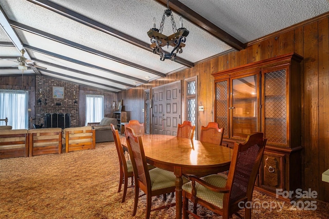 dining area featuring wood walls, lofted ceiling with beams, a brick fireplace, a textured ceiling, and carpet