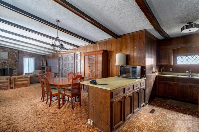 kitchen with pendant lighting, sink, vaulted ceiling with beams, a textured ceiling, and wood walls