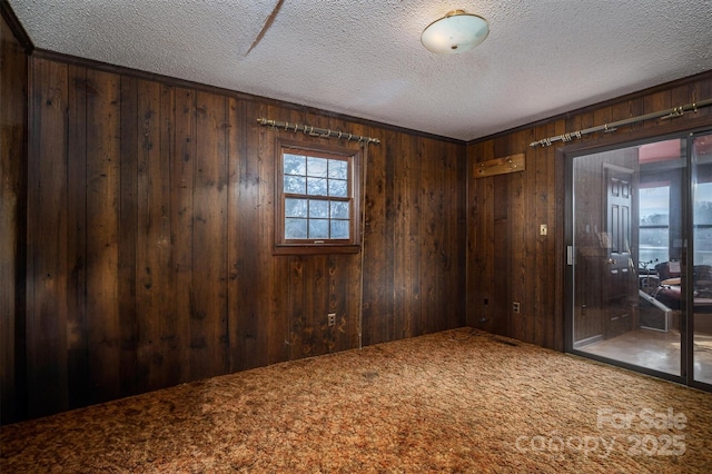 carpeted spare room with wooden walls and a textured ceiling