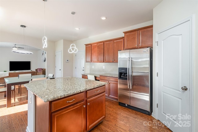 kitchen with pendant lighting, hardwood / wood-style flooring, stainless steel refrigerator with ice dispenser, light stone counters, and a kitchen island