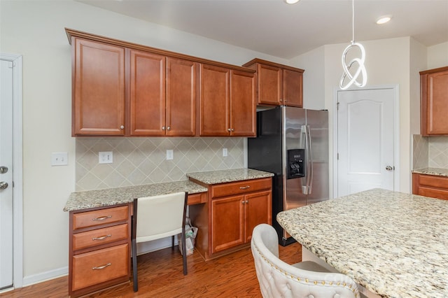 kitchen with a kitchen bar, built in desk, stainless steel fridge, pendant lighting, and hardwood / wood-style floors
