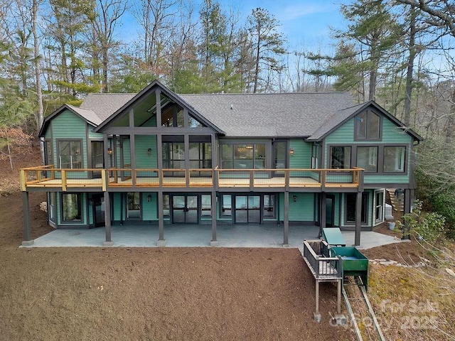 rear view of house featuring a patio area, a shingled roof, and a wooden deck