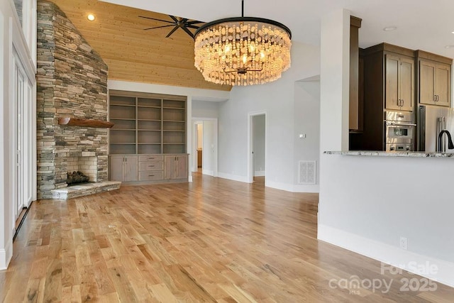 unfurnished living room with a towering ceiling, built in features, a fireplace, wood ceiling, and light wood-type flooring