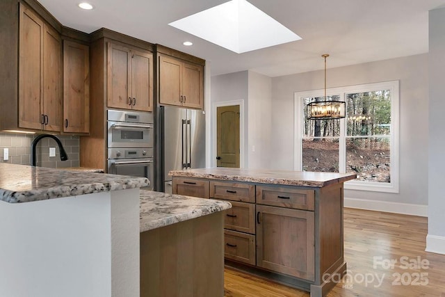 kitchen with a skylight, a center island, appliances with stainless steel finishes, light stone countertops, and backsplash