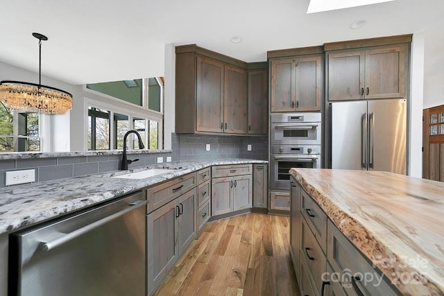 kitchen featuring sink, light hardwood / wood-style flooring, backsplash, stainless steel appliances, and light stone countertops