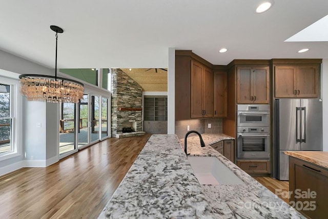 kitchen featuring stainless steel appliances, sink, pendant lighting, and light stone counters