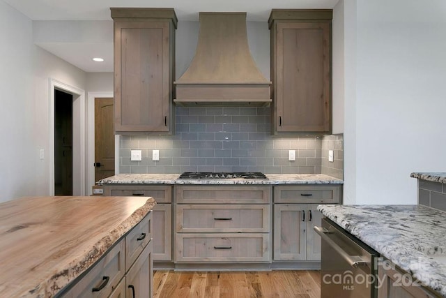 kitchen featuring stainless steel appliances, premium range hood, light stone counters, and light hardwood / wood-style floors