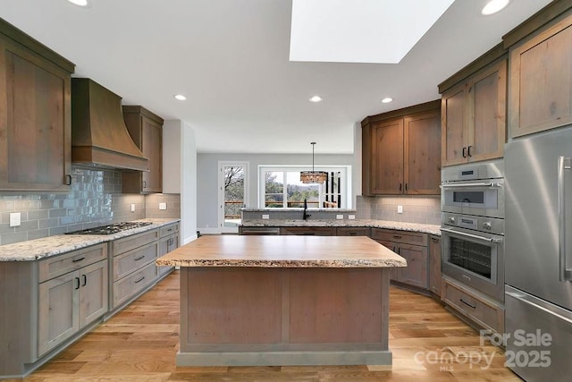 kitchen featuring light hardwood / wood-style flooring, stainless steel appliances, a kitchen island, decorative light fixtures, and custom exhaust hood