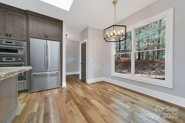 kitchen featuring dark brown cabinetry, hanging light fixtures, appliances with stainless steel finishes, light stone countertops, and light hardwood / wood-style floors