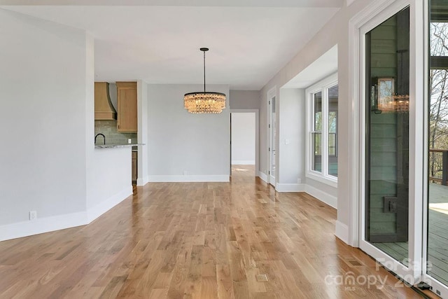 unfurnished dining area featuring an inviting chandelier, sink, and light hardwood / wood-style floors