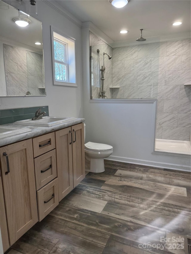 bathroom with crown molding, hardwood / wood-style flooring, vanity, a tile shower, and toilet