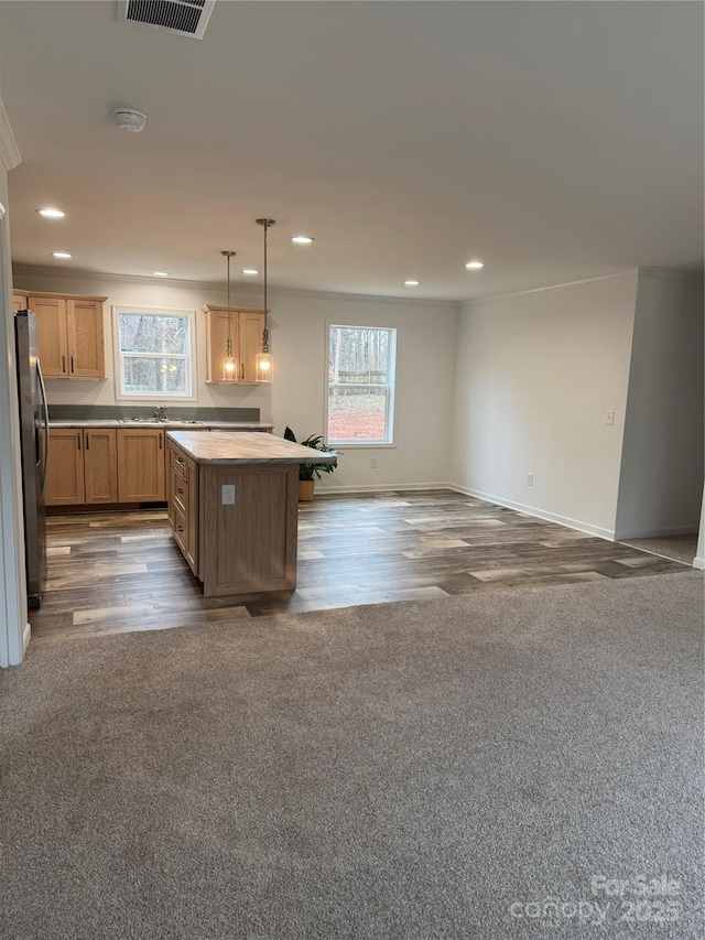 kitchen with a kitchen island, stainless steel refrigerator, decorative light fixtures, sink, and dark colored carpet