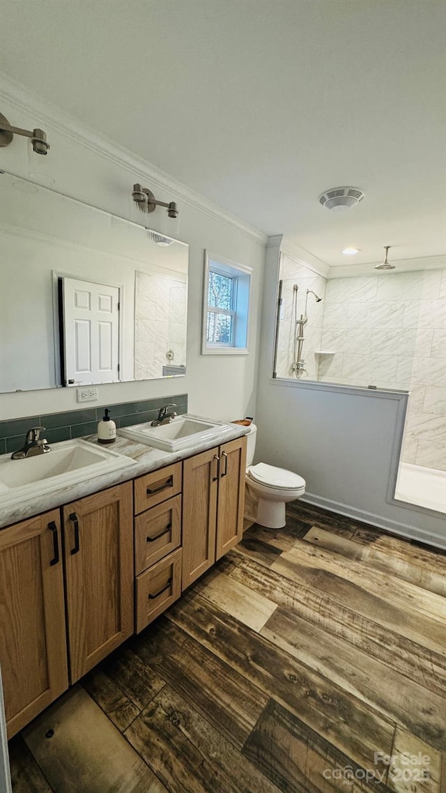 bathroom with a tile shower, hardwood / wood-style flooring, vanity, toilet, and crown molding