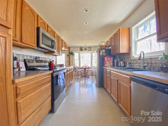 kitchen featuring brown cabinets, stainless steel appliances, tasteful backsplash, a sink, and a textured ceiling