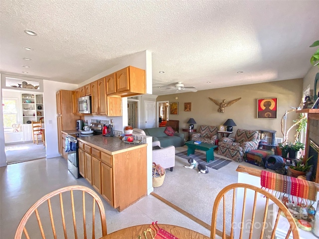 kitchen with a ceiling fan, appliances with stainless steel finishes, open floor plan, a textured ceiling, and a fireplace