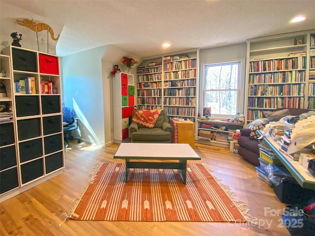 sitting room with bookshelves, a textured ceiling, and wood finished floors