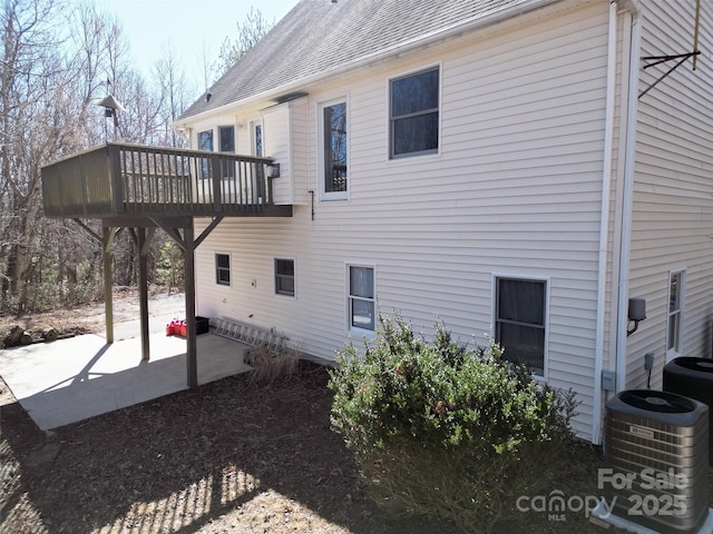 view of home's exterior with a deck, central AC unit, roof with shingles, and a patio area