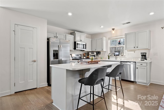 kitchen with a kitchen bar, white cabinetry, light wood-type flooring, appliances with stainless steel finishes, and a kitchen island