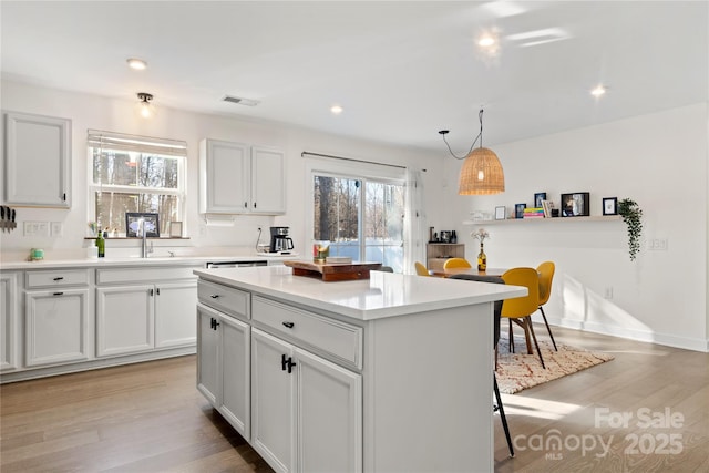 kitchen with decorative light fixtures, sink, white cabinets, a center island, and light wood-type flooring