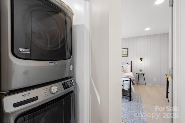 laundry room with stacked washer / dryer, wooden walls, and light hardwood / wood-style floors