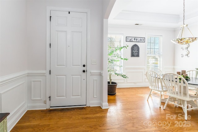 entryway with crown molding, wood-type flooring, and a tray ceiling