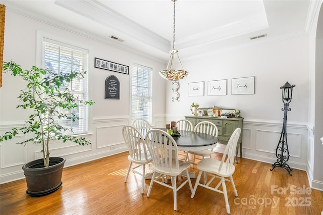 dining room featuring crown molding, light hardwood / wood-style floors, and a raised ceiling