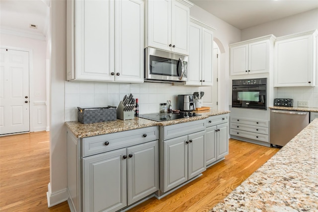 kitchen featuring tasteful backsplash, white cabinetry, gray cabinetry, light hardwood / wood-style floors, and black appliances