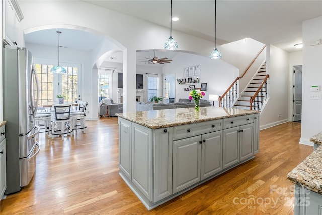 kitchen with light stone counters, decorative light fixtures, light hardwood / wood-style floors, and stainless steel refrigerator