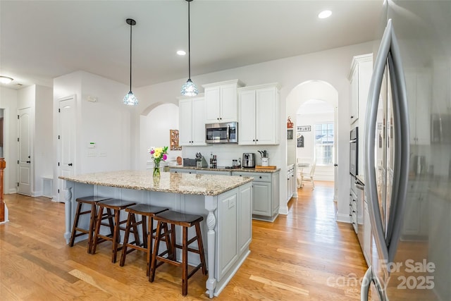 kitchen featuring hanging light fixtures, a kitchen island, stainless steel appliances, light stone countertops, and white cabinets