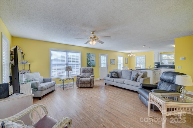 living room featuring ceiling fan with notable chandelier, a textured ceiling, and light wood-type flooring