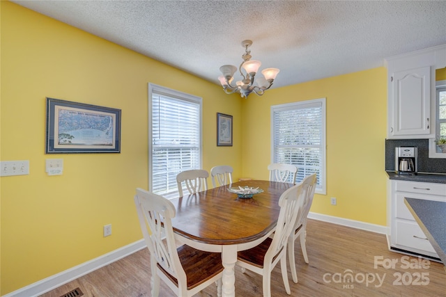 dining room with a chandelier, light hardwood / wood-style floors, and a textured ceiling