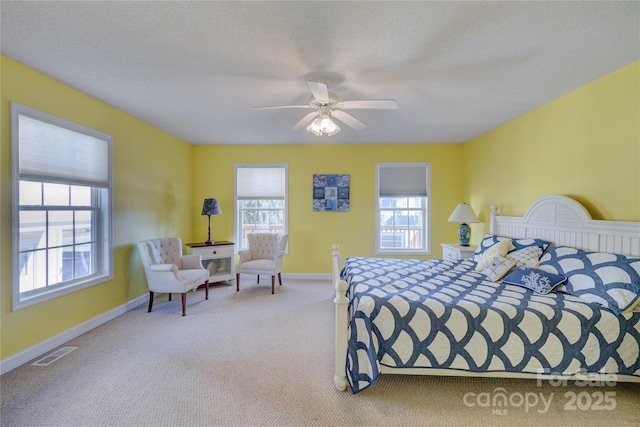 bedroom with ceiling fan, light colored carpet, multiple windows, and a textured ceiling