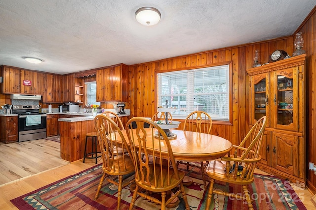 dining room featuring wood walls, a textured ceiling, and light wood-type flooring