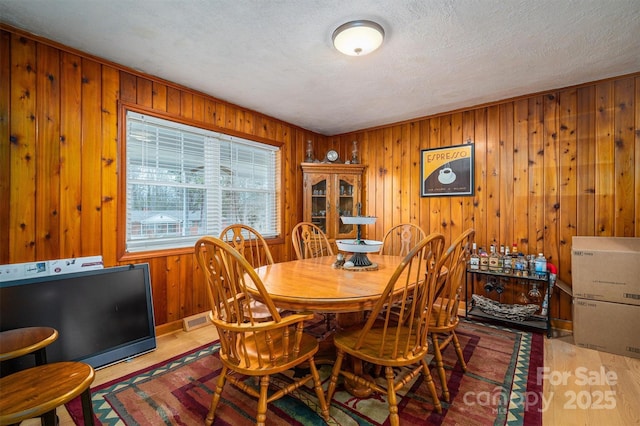 dining room featuring hardwood / wood-style flooring, a textured ceiling, and wood walls