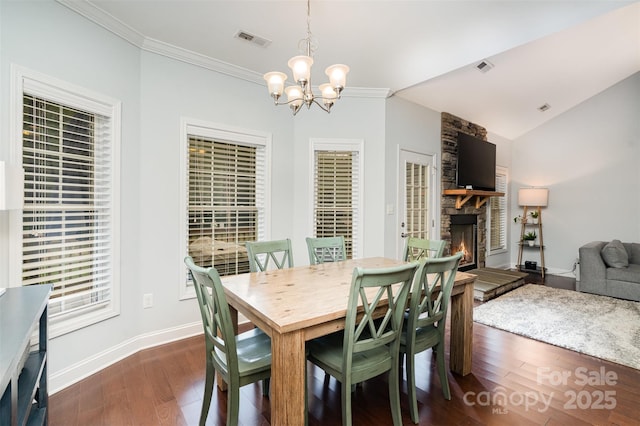 dining area with dark hardwood / wood-style flooring, a stone fireplace, ornamental molding, and a chandelier