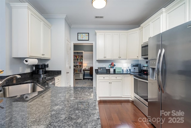 kitchen with sink, dark stone countertops, white cabinets, ornamental molding, and stainless steel appliances