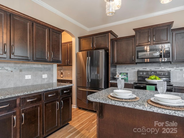 kitchen with stainless steel appliances, crown molding, light stone countertops, and dark brown cabinetry