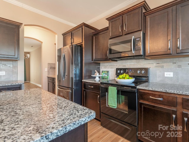 kitchen featuring dark brown cabinetry, light stone countertops, ornamental molding, and stainless steel appliances