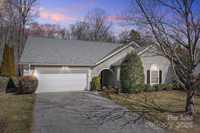 ranch-style home featuring a yard, a shingled roof, decorative driveway, and a garage