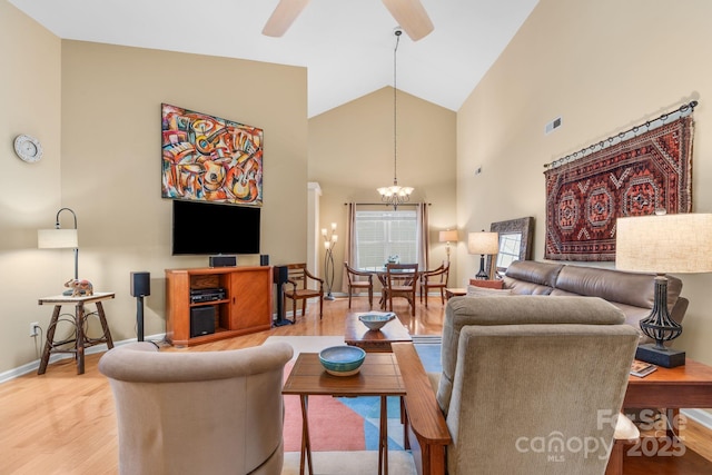 living room with visible vents, baseboards, light wood-type flooring, ceiling fan with notable chandelier, and high vaulted ceiling