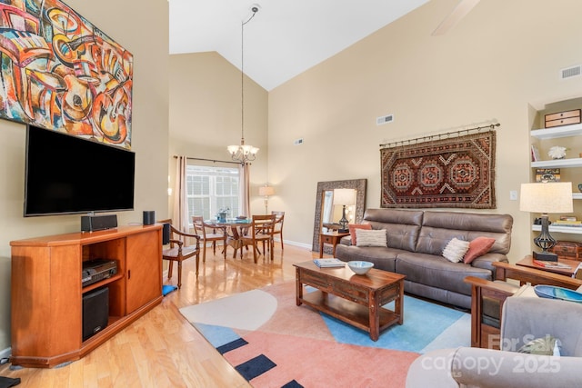 living area featuring a notable chandelier, wood finished floors, visible vents, and high vaulted ceiling