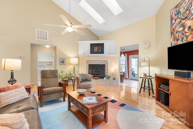 living room featuring visible vents, light wood finished floors, a skylight, ceiling fan, and a tile fireplace