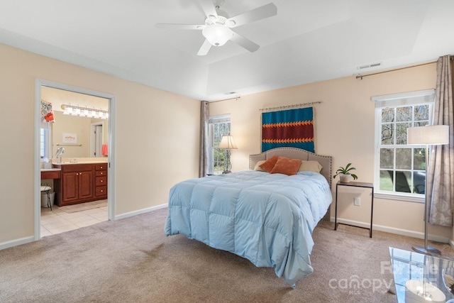 bedroom featuring visible vents, a tray ceiling, ensuite bath, baseboards, and light colored carpet