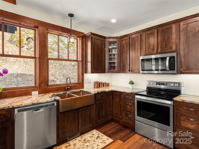 kitchen with sink, hanging light fixtures, stainless steel appliances, light stone countertops, and dark hardwood / wood-style flooring