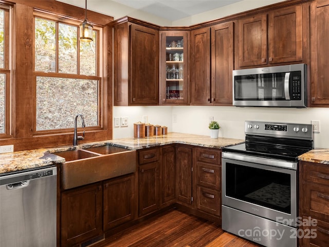 kitchen with appliances with stainless steel finishes, dark hardwood / wood-style floors, decorative light fixtures, sink, and light stone counters