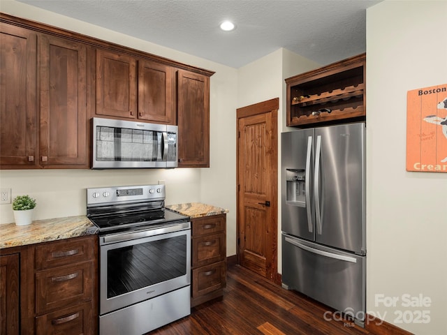 kitchen with stainless steel appliances, light stone countertops, dark hardwood / wood-style floors, and a textured ceiling