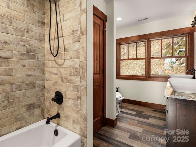 full bathroom with tiled shower / bath combo, vanity, wood-type flooring, and toilet