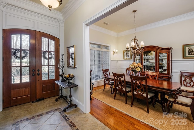 tiled entryway with crown molding, a notable chandelier, and french doors