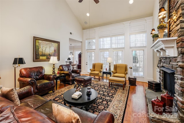 living room featuring a stone fireplace, wood-type flooring, high vaulted ceiling, and ceiling fan